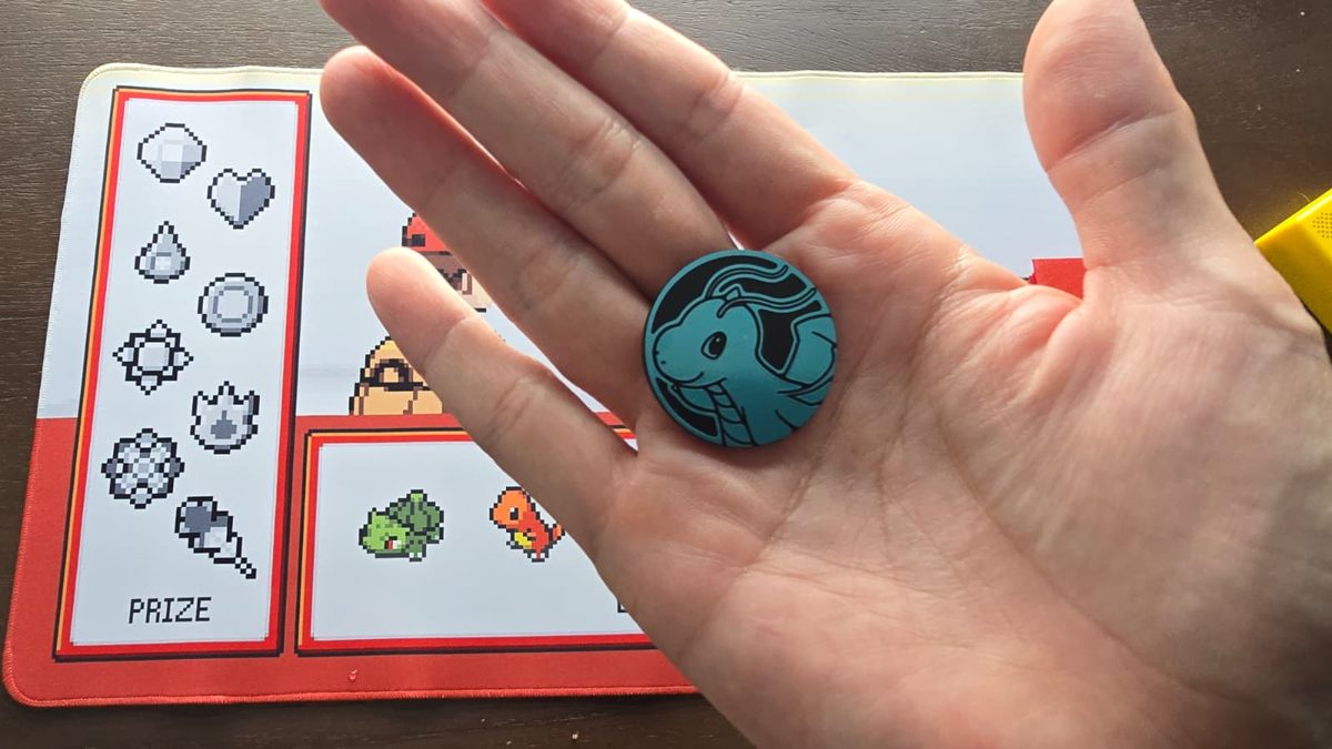 A teal Pokémon TCG coin showing the Pokémon side, held in a palm