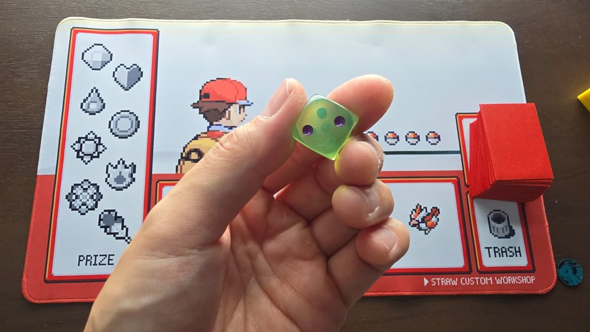 A translucent green die held between fingers, showing the 2 face