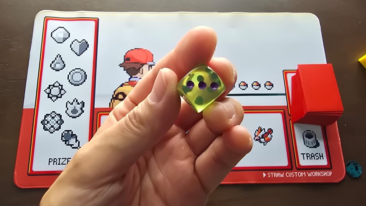 A translucent green die held between fingers, showing the 3 face