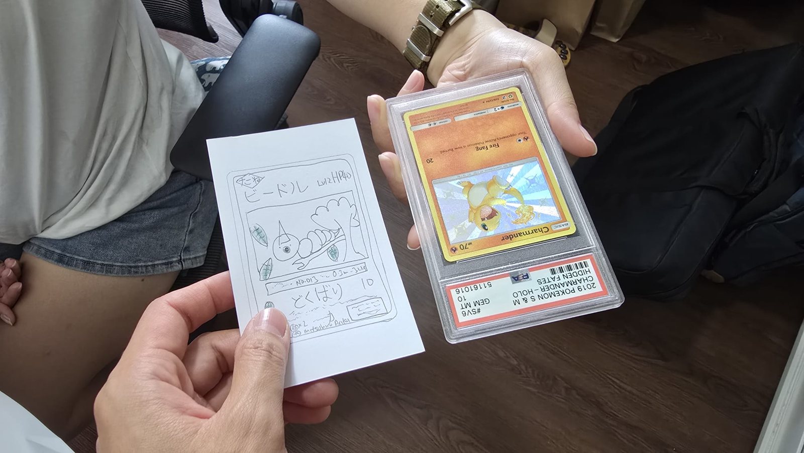 Two people mid-trade: one holds a hand-drawn Weedle card on white paper, the other holds a PSA 10 graded Charmander